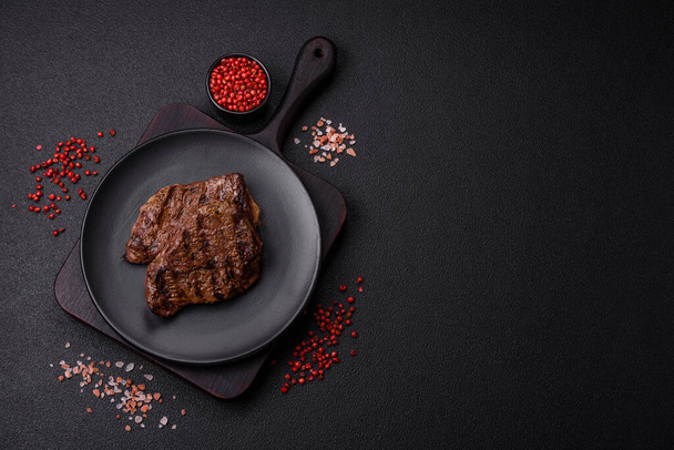 暗い背景に新鮮なジューシーなおいしい牛肉ステーキ.スパイスとハーブの肉料理 - 写真・画像