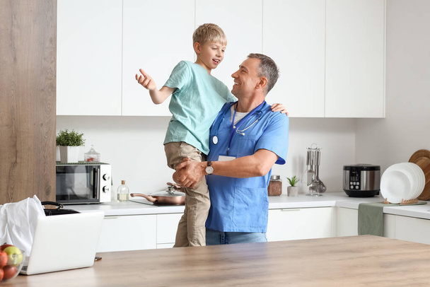 Reifer Arzt hält seinen kleinen Sohn in der Küche - Foto, Bild