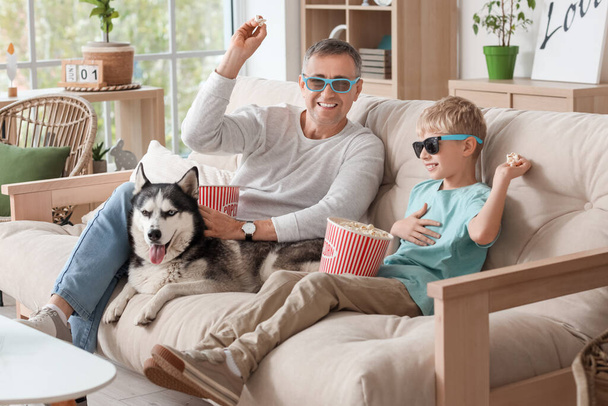 Médico maduro y su hijo pequeño en gafas 3D con palomitas para comer perros en casa - Foto, imagen