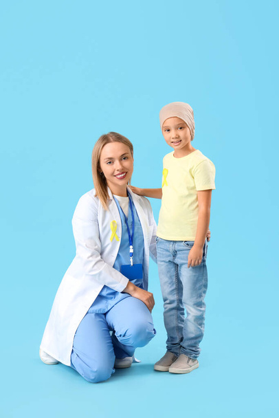 青い背景の医師との化学療法の後の小さなアジアの少女. 小児がん啓発コンセプト - 写真・画像