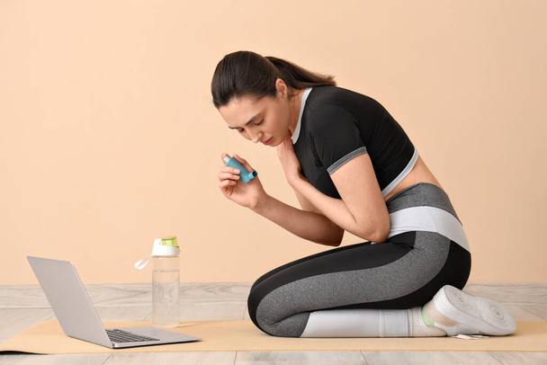 Jeune femme sportive avec inhalateur ayant une crise d'asthme près de la paroi beige - Photo, image