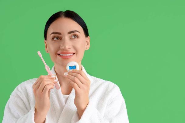 Linda jovem feliz mulher em roupão de banho com fio dental e escova de dentes no fundo verde - Foto, Imagem