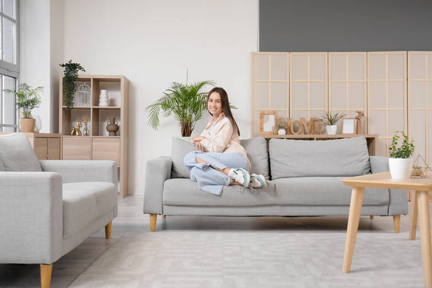 Pretty young woman sitting on grey sofa in living room - Photo, Image