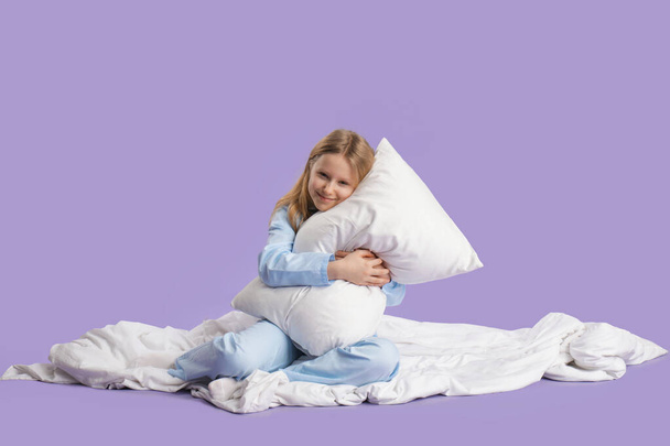 Adorable fille étreignant oreiller sur lit blanc sur fond lilas - Photo, image