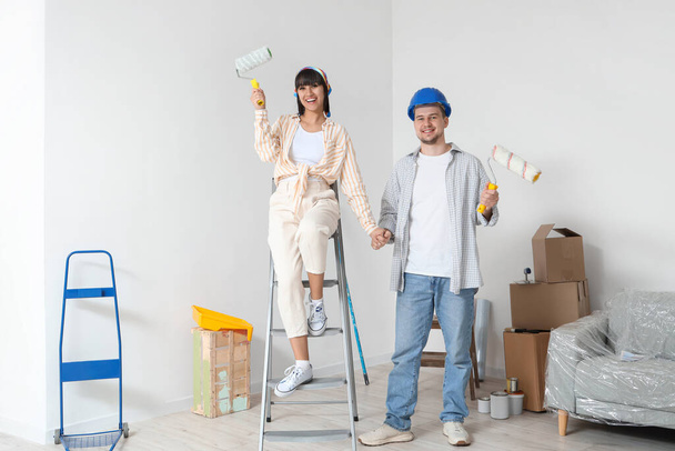 Yeni evlerinde tamirat sırasında boya silindirli genç bir çift. - Fotoğraf, Görsel