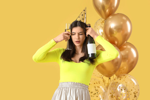Young woman with hangover and champagne after Birthday party on yellow background - Photo, Image