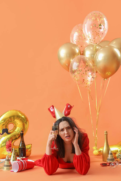 Young woman with hangover and champagne lying after Birthday party on orange background - Fotografie, Obrázek