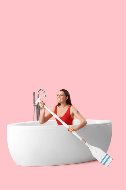 Vrouwelijke badmeester met peddel in badkuip op roze achtergrond - Foto, afbeelding