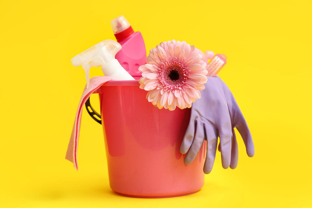 Bucket with cleaning supplies, tools and spring flower on yellow background - Photo, Image