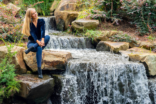Blondynka piękno świeci w oszałamiającym stroju upadku w pobliżu wodospadu parku, malownicza scena jesieni. - Zdjęcie, obraz