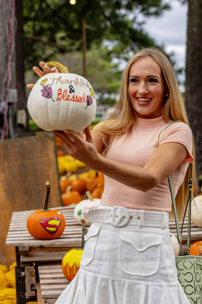 Eine schöne blonde Europäerin sucht ein paar Kürbisse und Blumen für die bevorstehenden Herbstfeste heraus - Foto, Bild