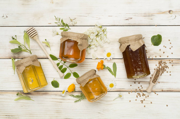 Jars with different types of honey on wooden background, top view - Photo, Image