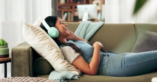Sluchátka, smartphone a asijské ženy ležící na pohovce pro streaming hudby, audioknihu nebo podcast v obývacím pokoji. Sluchátka, japonská dívka a telefon pro poslech audia, rádia nebo relaxaci o víkendu. - Záběry, video