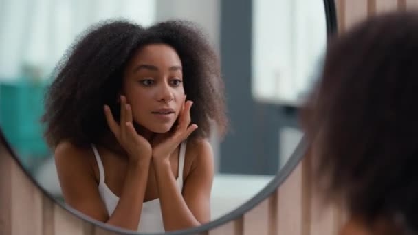 Tükröződés a fürdőszobában elég vonzó nő afro-amerikai lány női bőrápolás látszó megható arc segítségével krém hidratálja szépség kozmetikai ajkak hidratáló eljárás arcmasszázs - Felvétel, videó