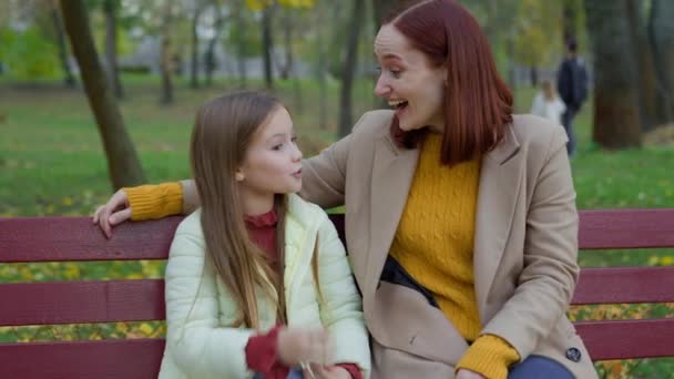 Happy Caucasian rodzina w parku jesień miasto na zewnątrz miejski na ławce rozmawianie matka kobieta mężczyzna z małą córką adoptowane dziecko dziewczyna rozmowa śmiech dzielenie się wiadomościami razem rozmowa śmiech bonding - Materiał filmowy, wideo