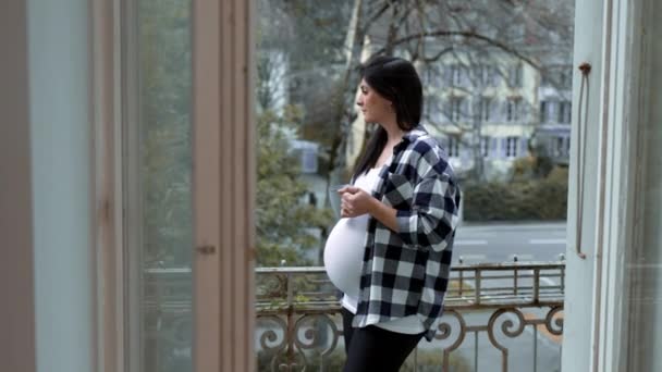 Pewna zamyślona ciężarna kobieta pijąca herbatę balkonem z widokiem na europejskie miasto, zrelaksowana kobieta ciesząca się widokiem z domu w trzecim trymestrze ciąży, spokojna kontemplacja - Materiał filmowy, wideo