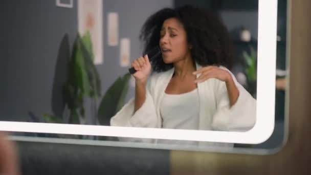 Gelukkig meisje in de badkamer hebben plezier gek dansen speels Afro-Amerikaanse vrouw haarverzorging krullend haar vrouw thuis kijken spiegel schoonheid dans doen alsof zingen in haarborstel kam als microfoon - Video