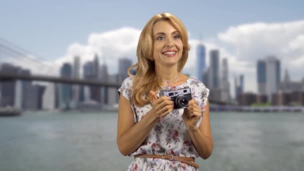 Portrait of a blonde woman with a retro photo camera. Big city river in the background. - Footage, Video
