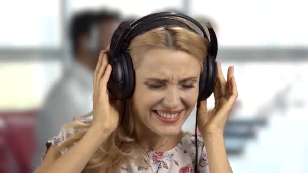 Portré egy nagyon boldog szőke nőről egy nagy fülhallgatóban és élvezi a zenét. Irodai belső tér a háttérben. - Felvétel, videó