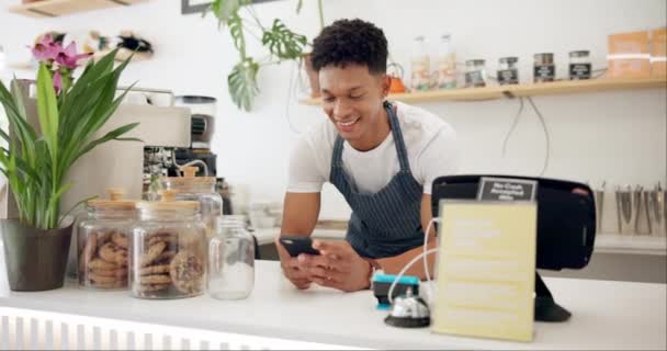 Man, cafe and barista with smile at phone for ecommerce, networking and communication at counter. Male person, small business and waiter with technology for online sale, funny discussion and service. - Footage, Video