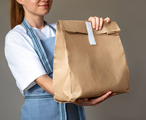 Коричневый бумажный пакет для еды на вынос в руках официантки. - Фото, изображение