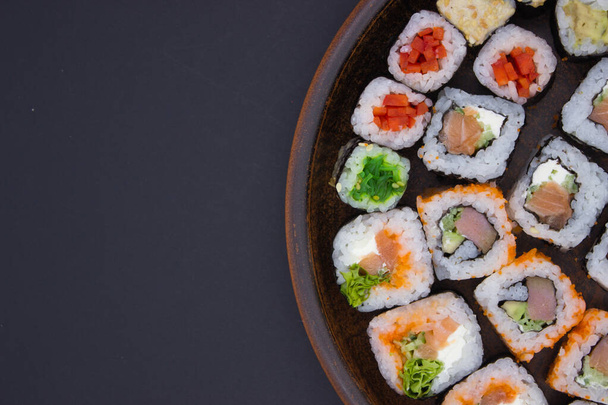 The photograph displays a creative sushi arrangement occupying one side of a round wooden platter, leaving the dark background to fill the rest of the frame. This off-center composition creates an engaging negative space that draws the eye to the det - Photo, Image