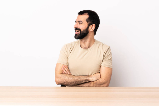 Homem caucasiano com barba em uma mesa olhando para o lado e sorrindo
. - Foto, Imagem