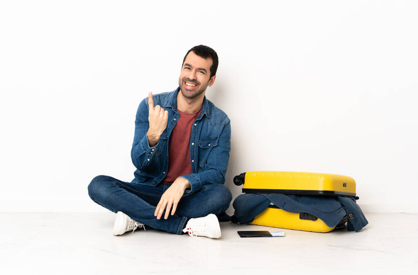 Blanc bel homme avec une valise pleine de vêtements assis sur le sol à l'intérieur faisant geste à venir - Photo, image