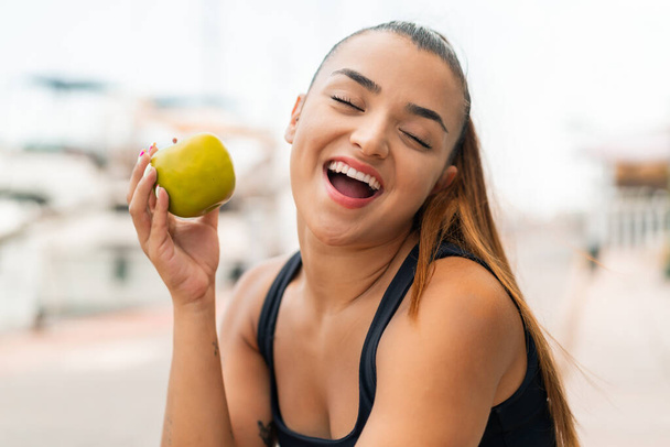 Junge hübsche Frau im Freien hält einen Apfel mit glücklichem Gesichtsausdruck - Foto, Bild