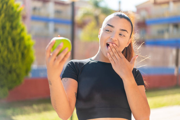 Young pretty brunette woman with an apple at outdoors with surprise and shocked facial expression - Photo, Image