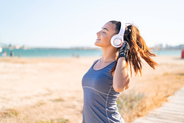 Junge hübsche Sportlerin trägt Sportkleidung und hört Musik mit Kopfhörern - Foto, Bild