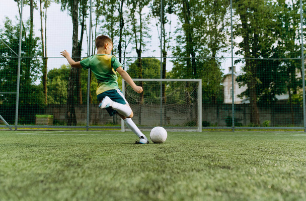 pieni jalkapalloilija potkaisee palloa maalia kohti. Poika pelaa jalkapalloa - Valokuva, kuva