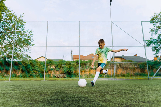 un pequeño jugador de fútbol patea la pelota en el gol. Niño jugando juego de fútbol - Foto, imagen