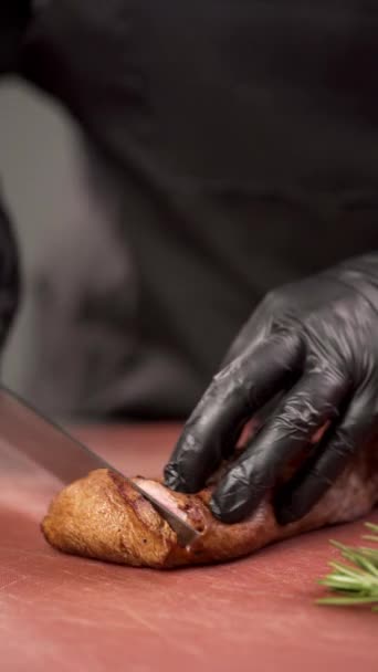 Процес різання яловичого стейка середній рідкісний з великим кухонним ножем на обробній дошці. нарізати м'ясо на шматки. Крупним планом рука кухарів. Вертикальне відео - Кадри, відео