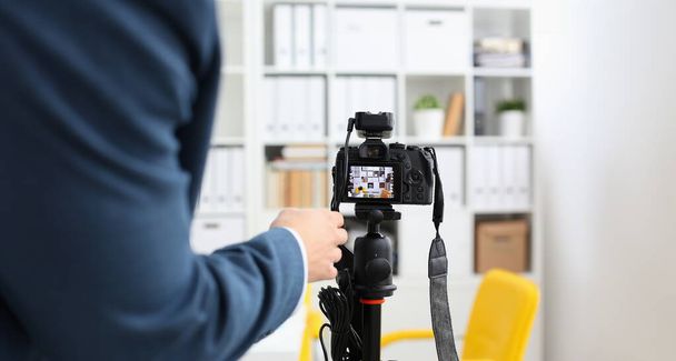 Male arms in suit mount camcorder to tripod making promo videoblog or photo session in office closeup. Vlogger adjust set up and check image quality to show job offer promotion selfie information - Photo, Image