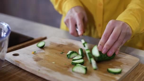 vrouw staan in de huiselijke moderne keuken bereiden van gezonde groentesalade. Kookplaat snijden komkommer in plakjes en het toevoegen in kom met salade. - Video