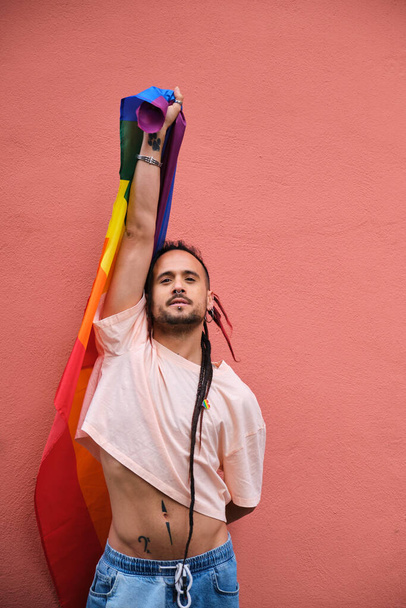 L'uomo gay con i dreadlock tiene una bandiera arcobaleno e sorride orgoglioso. Concetto di orgoglio e felicità. - Foto, immagini