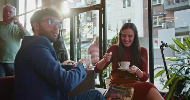 Twee vrienden delen een vreugdevol moment bij een kop koffie in een gezellige cafetaria, belichamen de warmte van vriendschap en casual sociale interacties, creëren een comfortabele sfeer. - Video