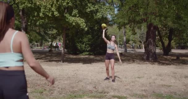 Két fiatal nő élvezi a barátságos fogási játék egy rögbi labda a parkban egy napsütéses napon. - Felvétel, videó