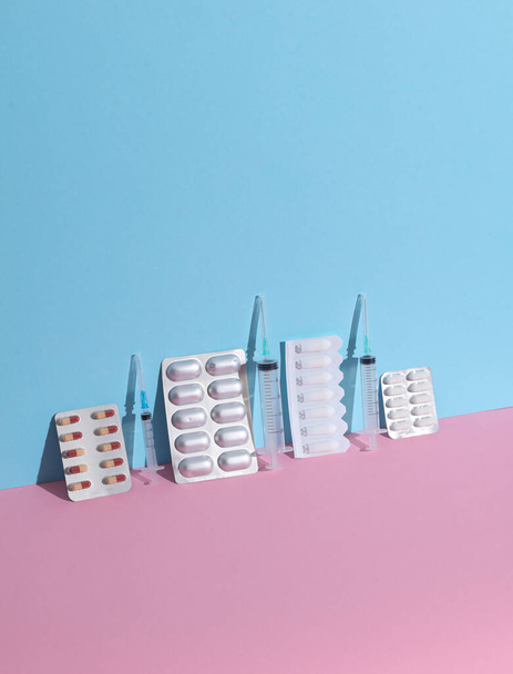Vários medicamentos, bolhas de comprimidos com seringas em um fundo azul-rosa. Layout criativo, conceito de medicina minimalismo - Foto, Imagem