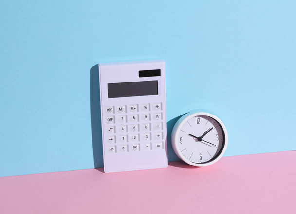 Biały kalkulator z zegarem na niebiesko-różowym tle z cieniem. Koncepcja biznesu i finansów. Kompozycja kreatywna - Zdjęcie, obraz
