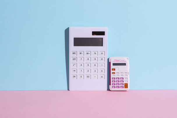 Twee rekenmachines op blauwroze achtergrond met schaduw. Bedrijfs- en financieel concept. Creatieve indeling - Foto, afbeelding