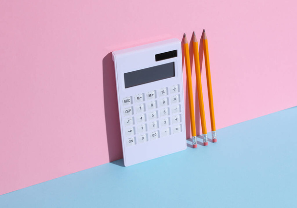 Calculator en potloden op een blauw-roze pastelachtergrond. Onderwijs- of bedrijfsconcept - Foto, afbeelding