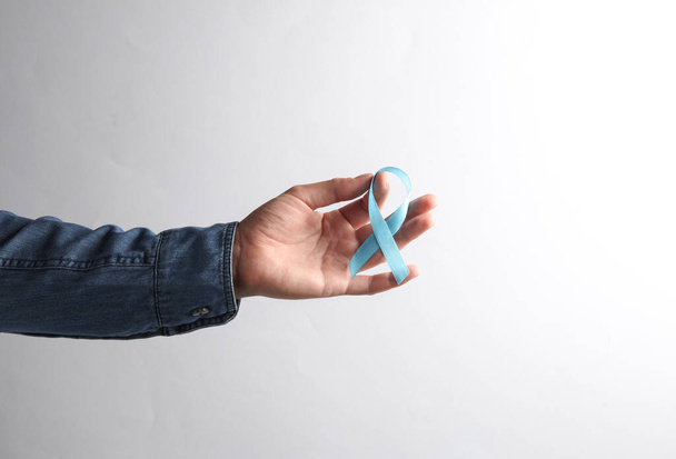 Чоловіча рука в джинсовій сорочці, що тримає синю стрічку обізнаності про рак простати на сірому фоні - Фото, зображення