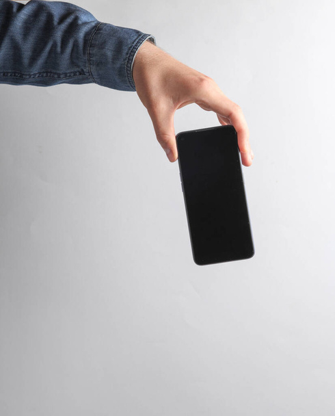 Hand in Jeanshemd mit Smartphone vor grauem Hintergrund - Foto, Bild