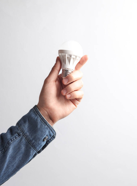 Man's hand in denim shirt holding light bulb on gray background. Idea, business concept - Photo, Image
