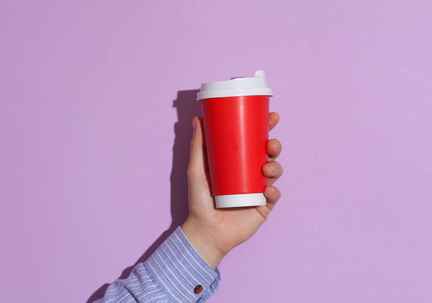 Man's hand in shirt holding red cardboard coffee cup on purple pastel background with shadow - Photo, Image
