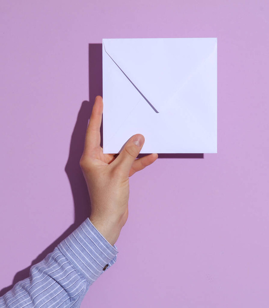 Рука людини в сорочці, що тримає білий конверт на фіолетовому тлі. Макет для дизайну - Фото, зображення