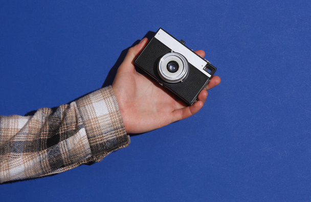 Ανδρικό χέρι σε πουκάμισο με ρετρό κάμερα σε μπλε φόντο με σκιά - Φωτογραφία, εικόνα
