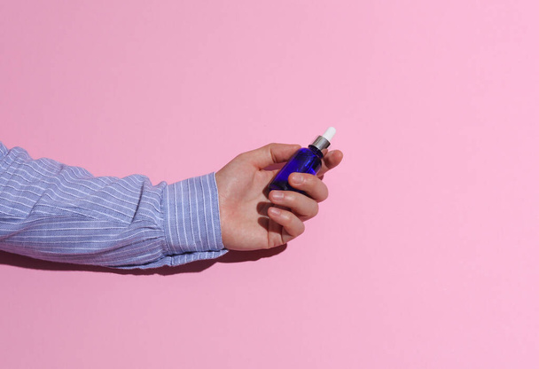 Man 's hand in een shirt met serumfles op roze achtergrond - Foto, afbeelding